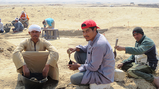 Workers crouch in the sand.