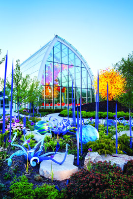 a garden full of glass sculptures with a green house in the background