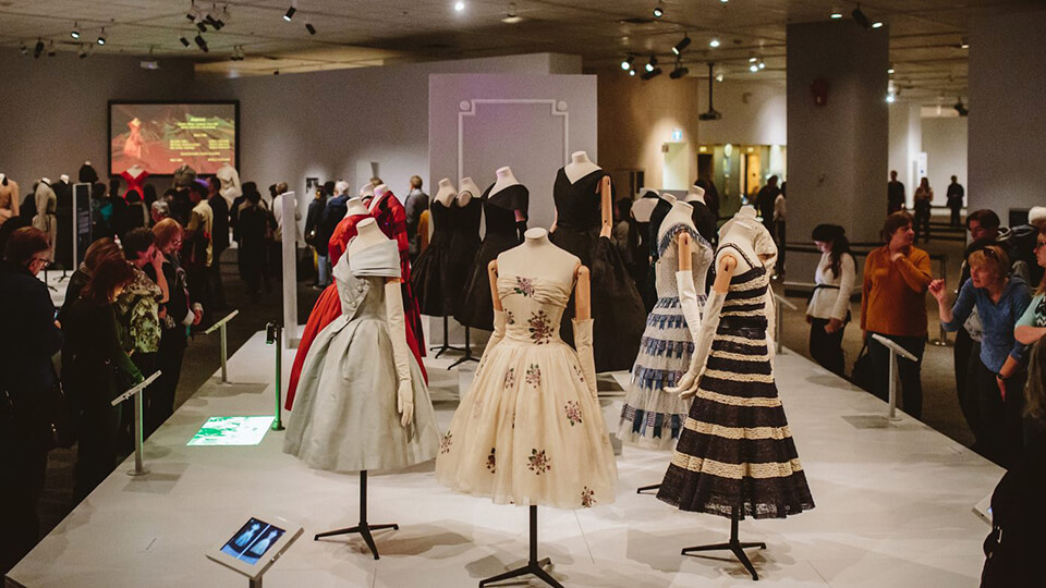 Dior dresses on display in museum space.