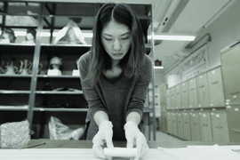 Black and white photograph of a woman wrapping an artifact in protective paper for shipping