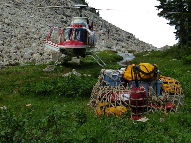 Helicopter at campsite with a load of equipment still in its net.