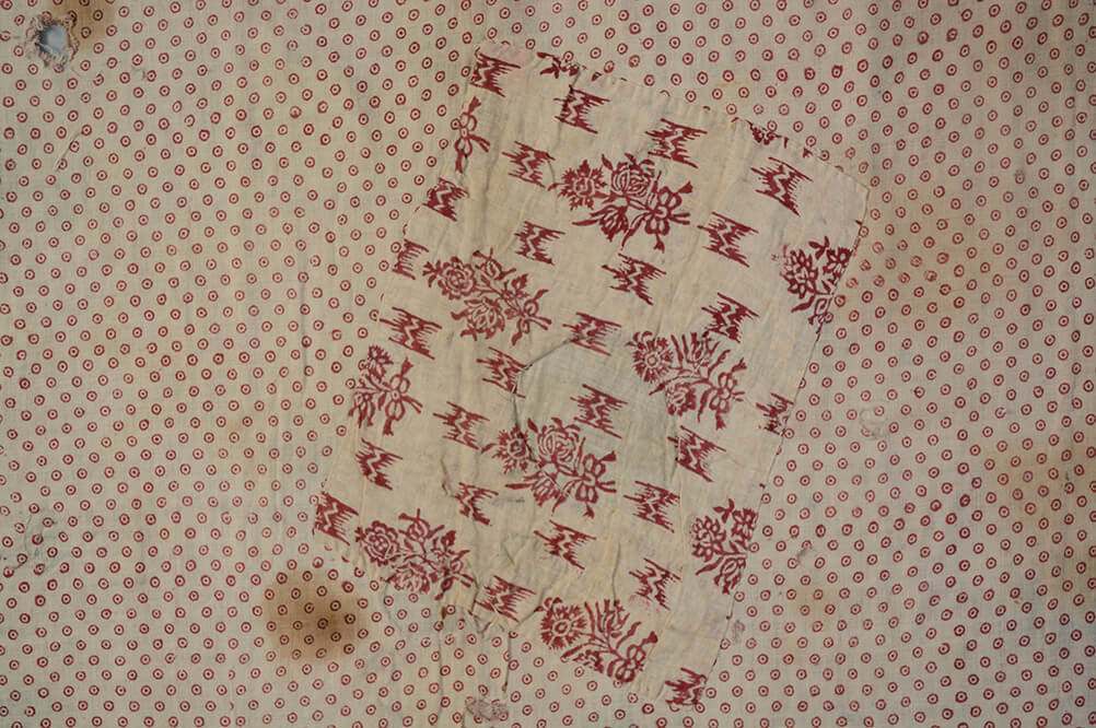 A detail of the reverse of the cope showing a large rectangular patch of red and white floral fabric stitched to the lining.
