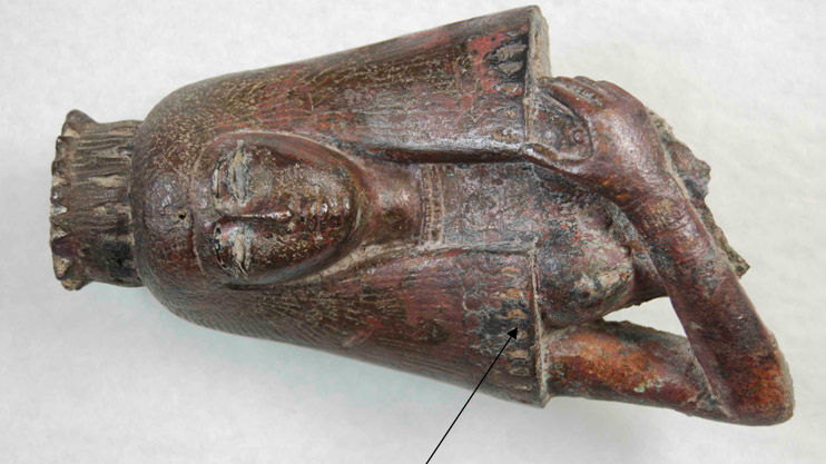 Detail of upper torso after cleaning. Location of gilding (photo: Franziska Schlicht) Artifact lying on its side with an arrow pointing to the location of the oiginal guilding found on the headdress.