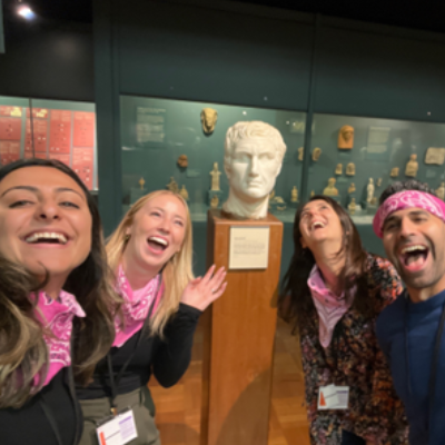 Four visitors laughing and smiling while standing in front of a Greek marble bust.