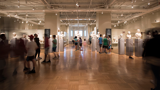 View in the Eaton Gallery of Rome with visitors shows visitors walking and looking at the Roman Busts on display.