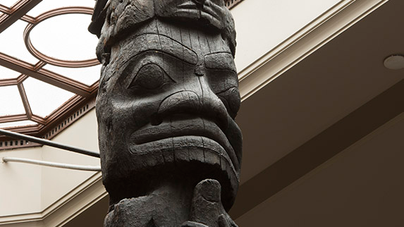 Close up of the top of a totem pole with a skylight behind it.