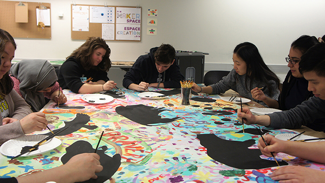 Youth Cabinet members work on a collaborative painting of the Seven Grandfather Teachings.
A group of Youth Cabinet members paint at a table onto canvas.