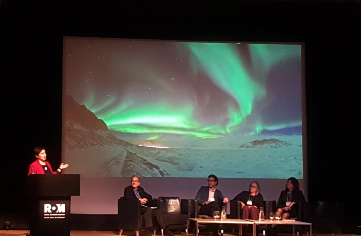 Sandra Inutiq standing on stage at the ROM speaking to audience alongside four other panelists. 