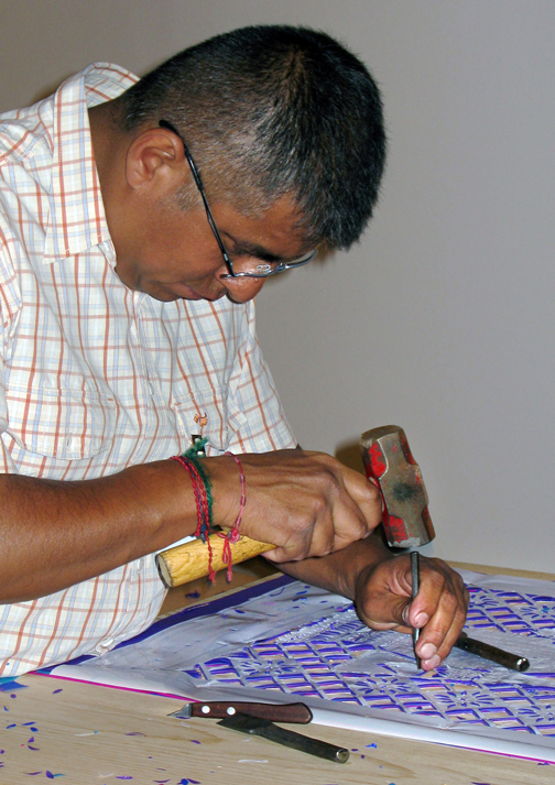 Sergio is chiselling patterns into a stack of paper with a wooden board as support.