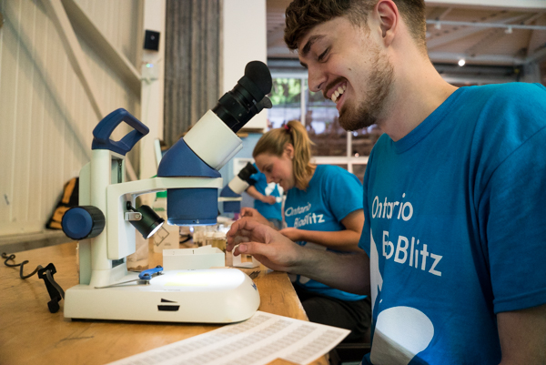 Roegan Vetro looking through a microscope in a room full of people