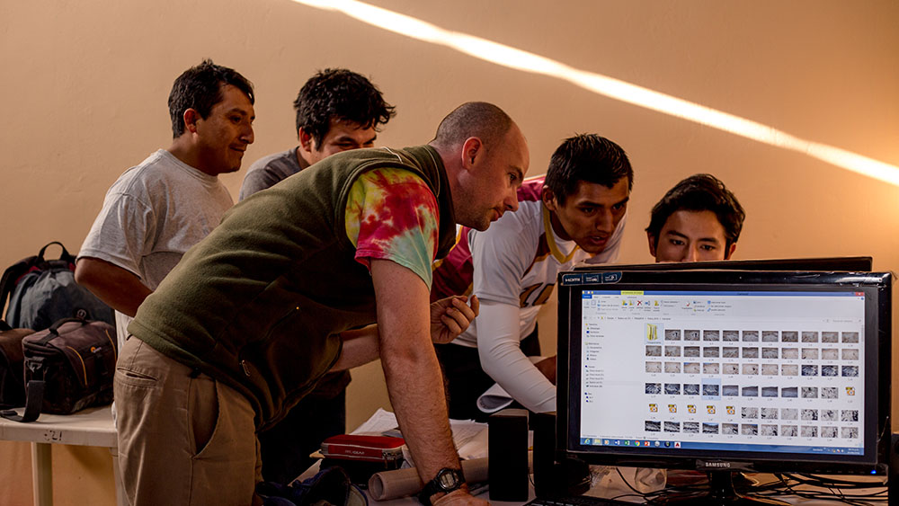 Researchers gather around a computer set up in the field to analyze work.