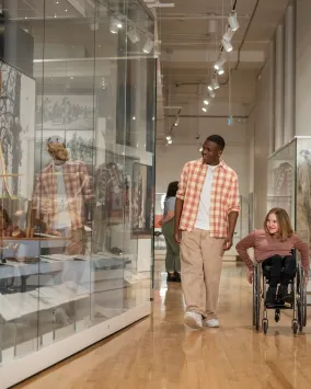 Un homme en chemise à carreaux marchant avec une fille en fauteuil roulant et regardant les collections du musée ROM.