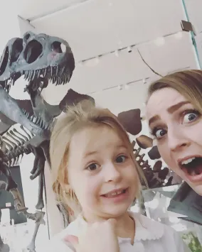 A young woman and a child pretend to be scared in front of a T.rex skeleton