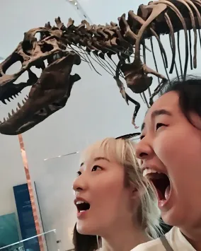 Two girls pretend to be scared in front of a T.rex skeleton