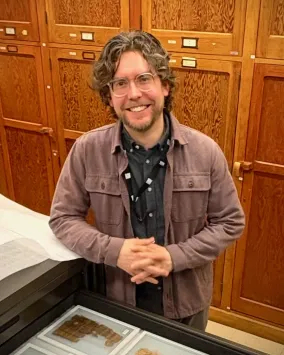 Dr. Gregory Fewster standing with clasped hands in front of museum drawers.