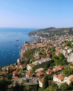 A picturesque coastal town with numerous buildings, and a beautiful, calm sea with several boats.