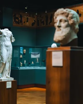 Ancient Greek statues and marble reliefs displayed in a museum gallery.