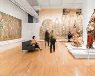 A woman sits still and enjoys a moment taking in ROMs Chinese temple art while other people move around her.