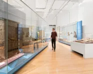 A person walks through a gallery admiring the large furniture in glass cases/