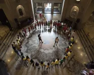 La caméra regarde de haut un groupe d'étudiants assis en cercle au fond d'une salle ronde ornée.