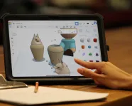 A hand touches an ipad displaying 3D models of Egyptian objects