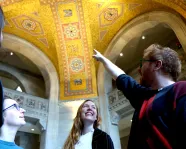 Three happy people look up at an ornate golden ceiling as one person points out a detail.