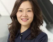 Portrait of a smiling woman with long wavy hair wearing a dark blue button-up shirt.
