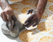 Hands pressing a stamp with yellow paint onto white fabric.