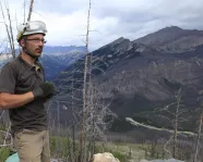Jean-Bernard Caron debout sur une colline avec des montagnes en arrière-plan
