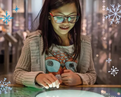 Une jeune fille regarde fixement et sourit avec émerveillement en interagissant avec un écran dans le musée.