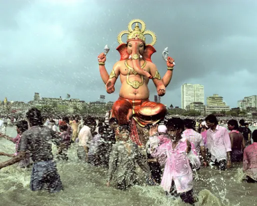 Ganapati Immersion People walking through water. In the center and high above the crowd is a respected figure in seated position with four arms/hands. The face is an elephant.
