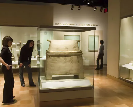 Two people examine a sarcophagus in a gallery, one leans forward to get a closer look at the details.