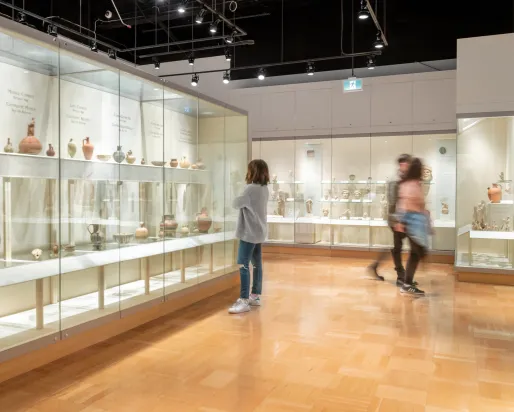 Three people walk around a gallery filled with ancient pottery in cases.