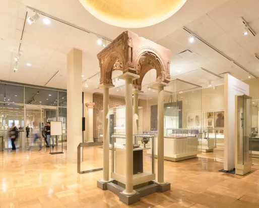 An ancient archway supported by modern pillars above a case containing a goblet and bowl.