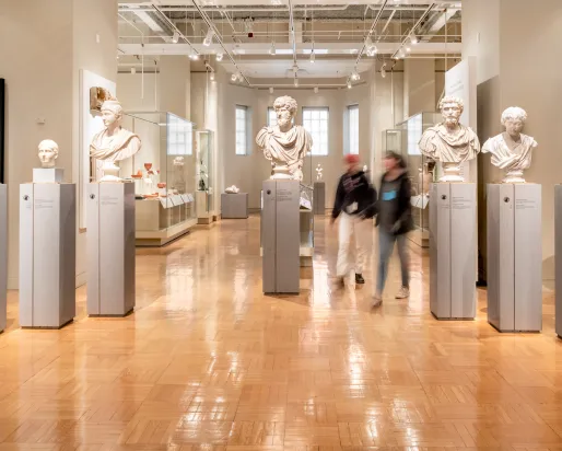 Two people walk among the marble busts of important Romans.
