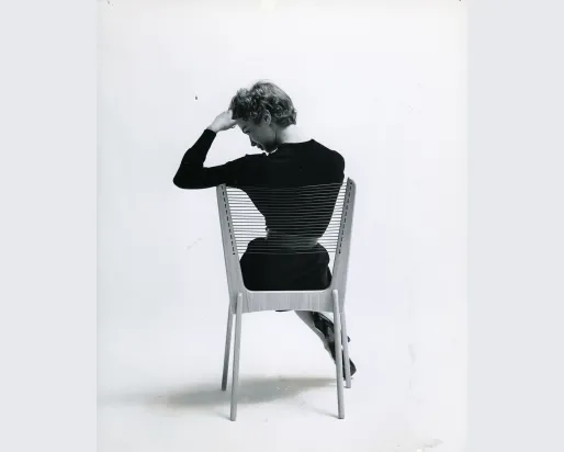 A woman seated on a chair, facing away from the camera, with her back visible in the image.