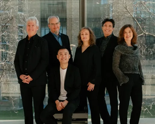 Six musicians in dark clothing, gathered in a group photograph.