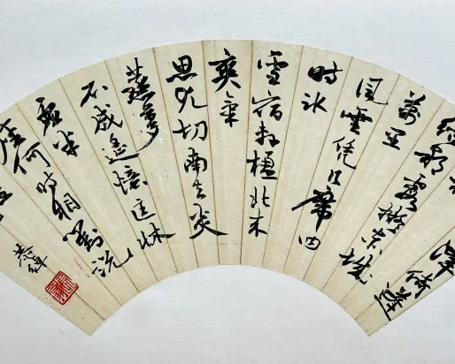 Fan-shaped artwork featuring traditional Chinese calligraphy in bold black ink on a cream background, with a red seal stamp