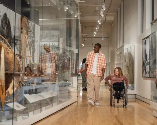 A guy in a plaid shirt walking with a girl in a wheelchair looking at museum collections at ROM