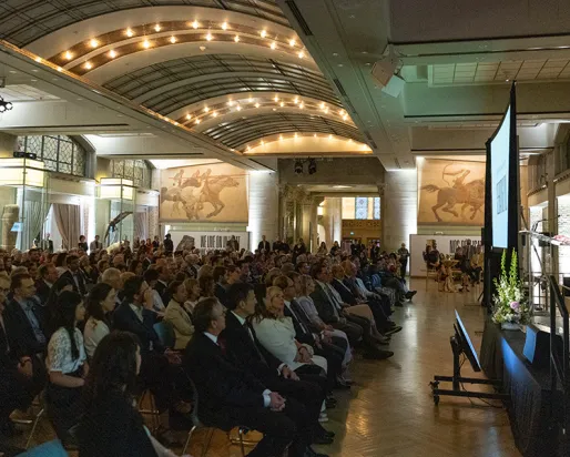 Audience of people seated, listening to a speaker on stage