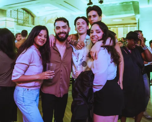A group of people posing in a crowd with a green lighting in the background.