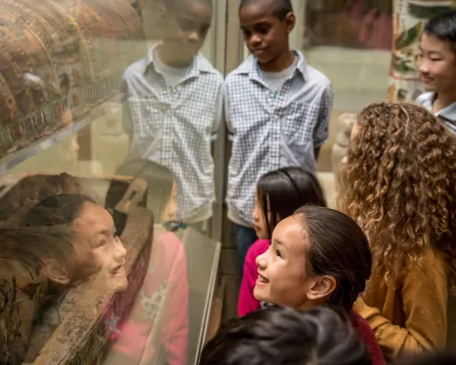 Children looking at an ancient Egyptian mummy display in a museum exhibit.