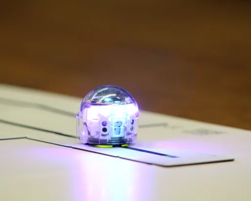 A small silver robot rolls along a dark track on a paper