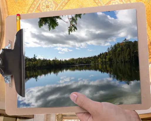A hand holds a clipboard in front of a gallery at ROM. The clipboard displays an image of a glassy lake ringed by trees
