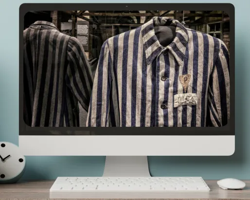 A computer monitor on a desk displays an image of prisoner uniforms from Auschwitz