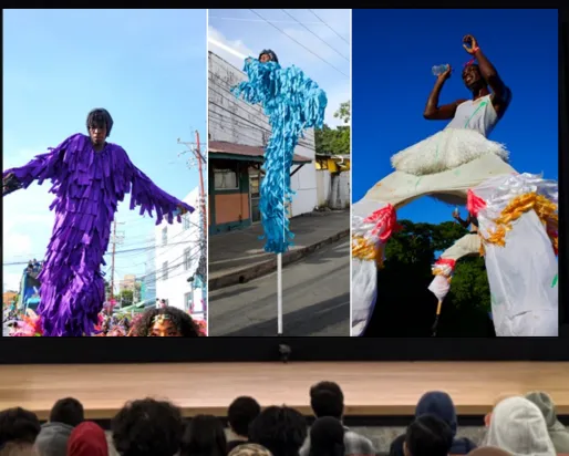 A presenter on a stage in front of an audience stands behind a podium labelled ROM. The screen next to them displays a composite image of three dark-skinned people wearing colourful fringed outfits and walking on stilts.