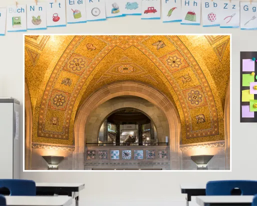 A screen in a classroom displays an image of a golden mosaic ceiling surrounding an arched balcony, through which a rhino in a case can be seen