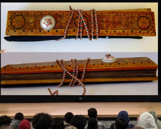 A smiling man stands behind a podium labelled ROM on a stage and gestures at a screen as an audience watches. The screen displays two images of a manuscript held between two ornately decorated wooden covers.