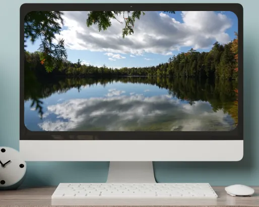A computer screen on a desk displays an image of a glassy lake ringed by trees