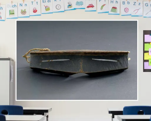 A colourful classroom with a display screen at the front. The screen shows iggaak (snow goggles) carved from wood with narrow horizontal slits for the eyes, and a string at the back.
